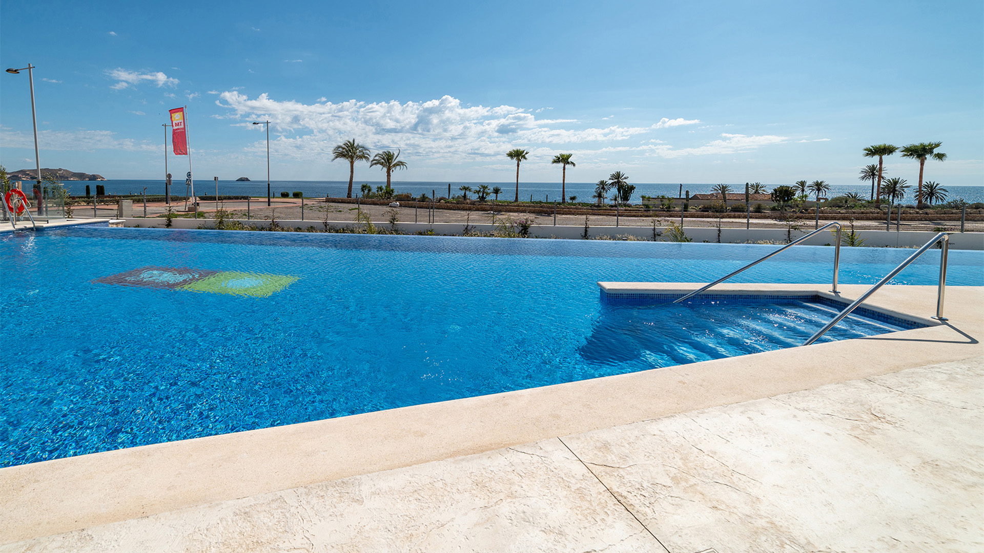 Grote gemeenschappelijke zwembadzone met ligbedden en palmbomen