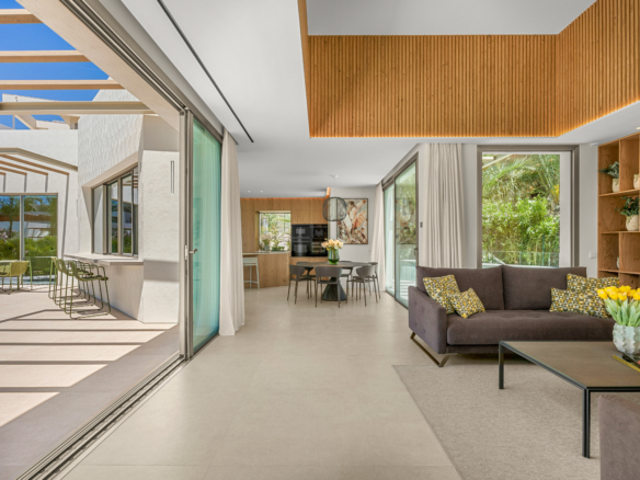 Open-concept living room with a gray sofa, geometric cushions, wood shelving, and wide glass doors to an outdoor patio.