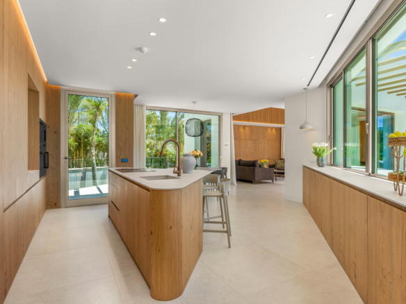 Bright, modern kitchen with warm wood cabinets, a large island with a sink, and glass doors opening to a garden.