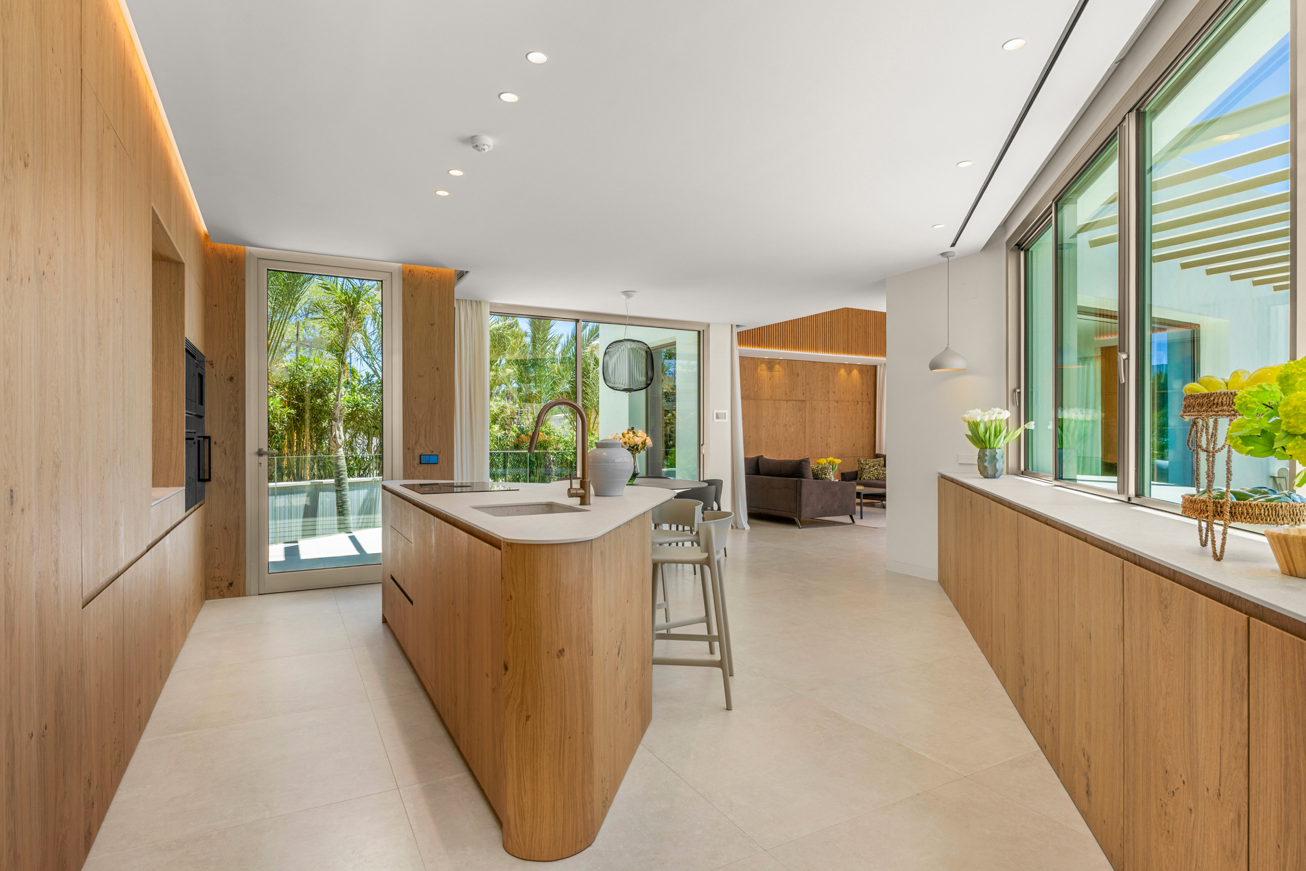 Bright, modern kitchen with warm wood cabinets, a large island with a sink, and glass doors opening to a garden.