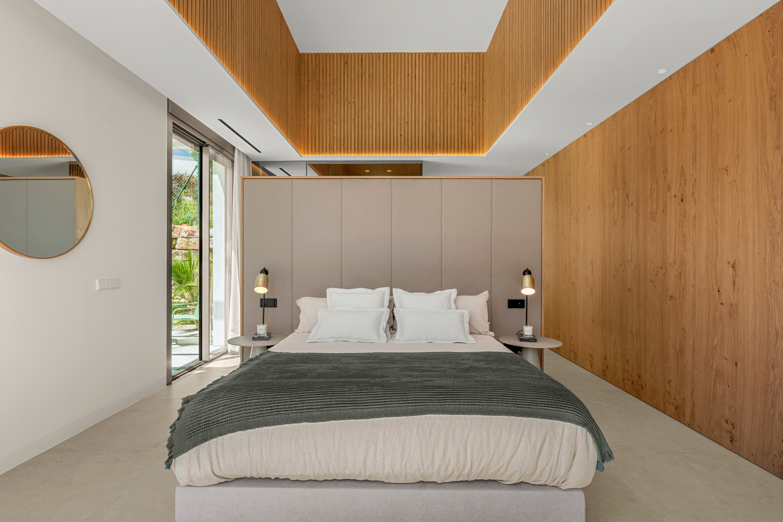 Modern hotel bedroom with a beige upholstered headboard, white bedding, gray throw, and warm wood paneling along the walls.] , but (this is wrong)