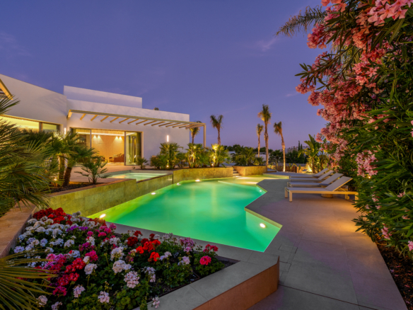 Luxe villa Las Colinas met verlicht zwembad, bloemen en mediterrane tuin in de avond