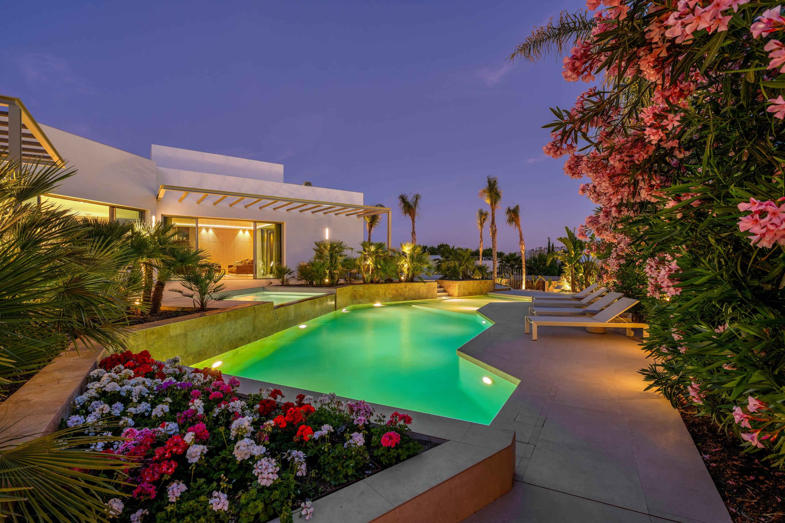 Luxe villa Las Colinas met verlicht zwembad, bloemen en mediterrane tuin in de avond