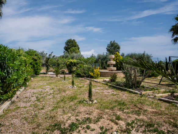 Sunny garden scene with gravel paths, lush shrubs, and a tiered stone fountain under a blue sky.