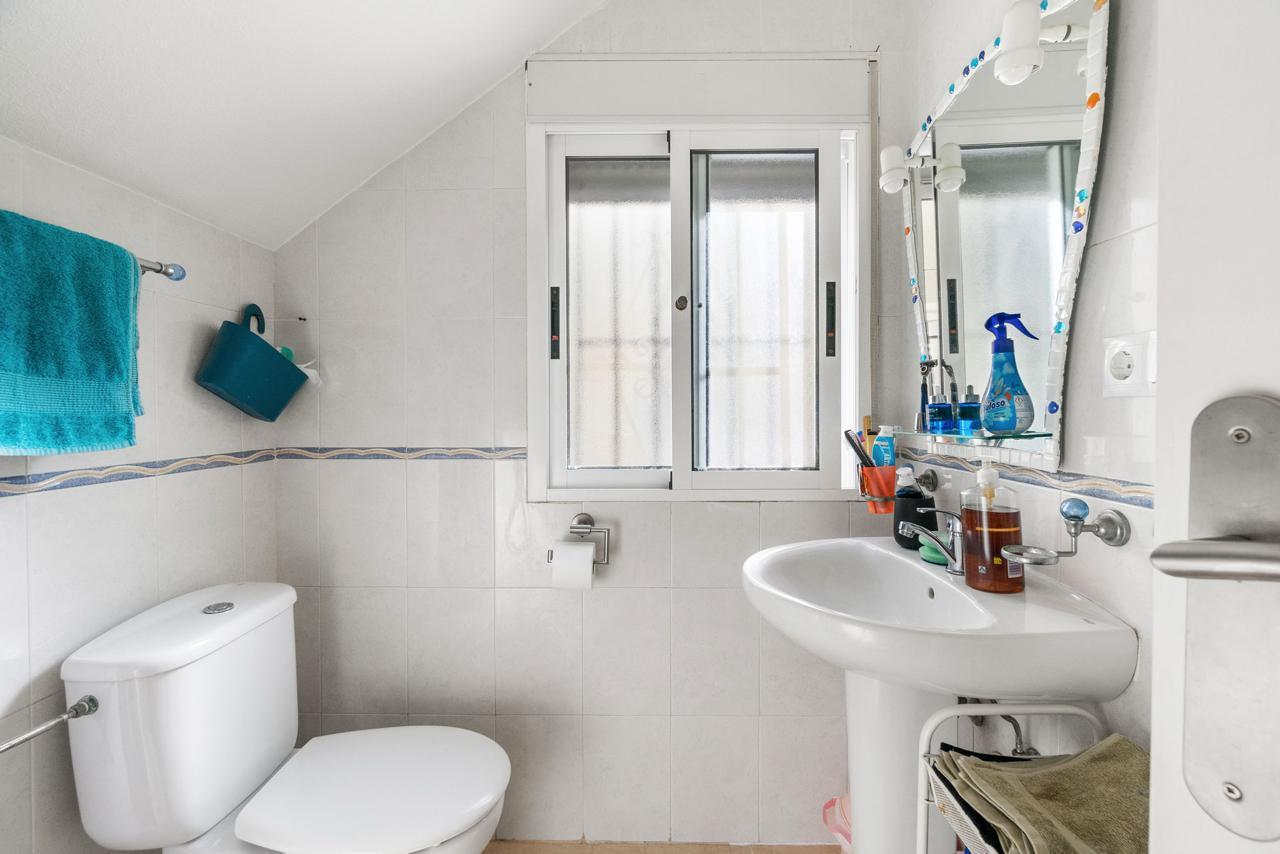 Small white bathroom with a toilet, pedestal sink, and a window above the sink; blue towel hangs on the wall.