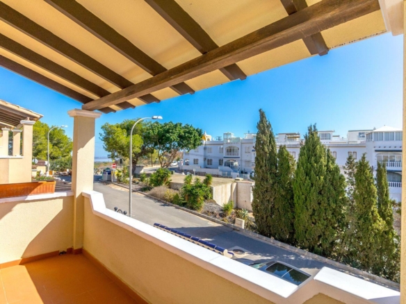 Terrace view with yellow walls and dark wooden beams, overlooking a street with white buildings and green trees against a bright blue sky.