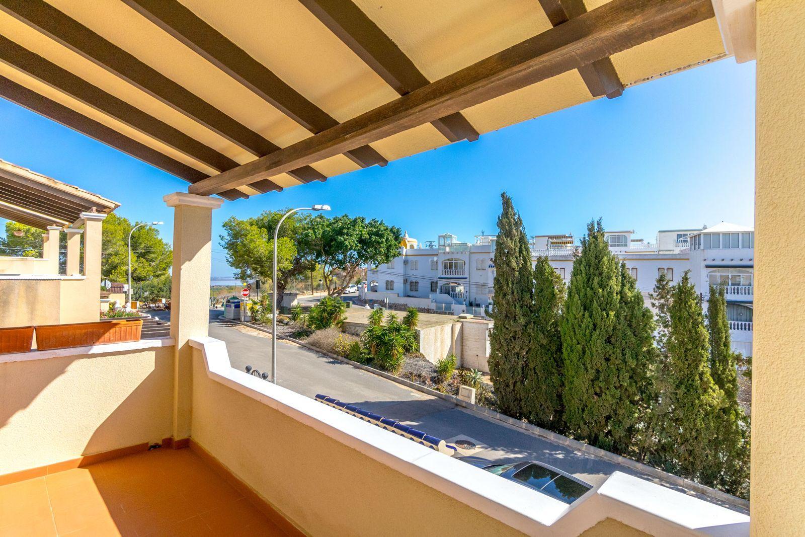 Terrace view with yellow walls and dark wooden beams, overlooking a street with white buildings and green trees against a bright blue sky.