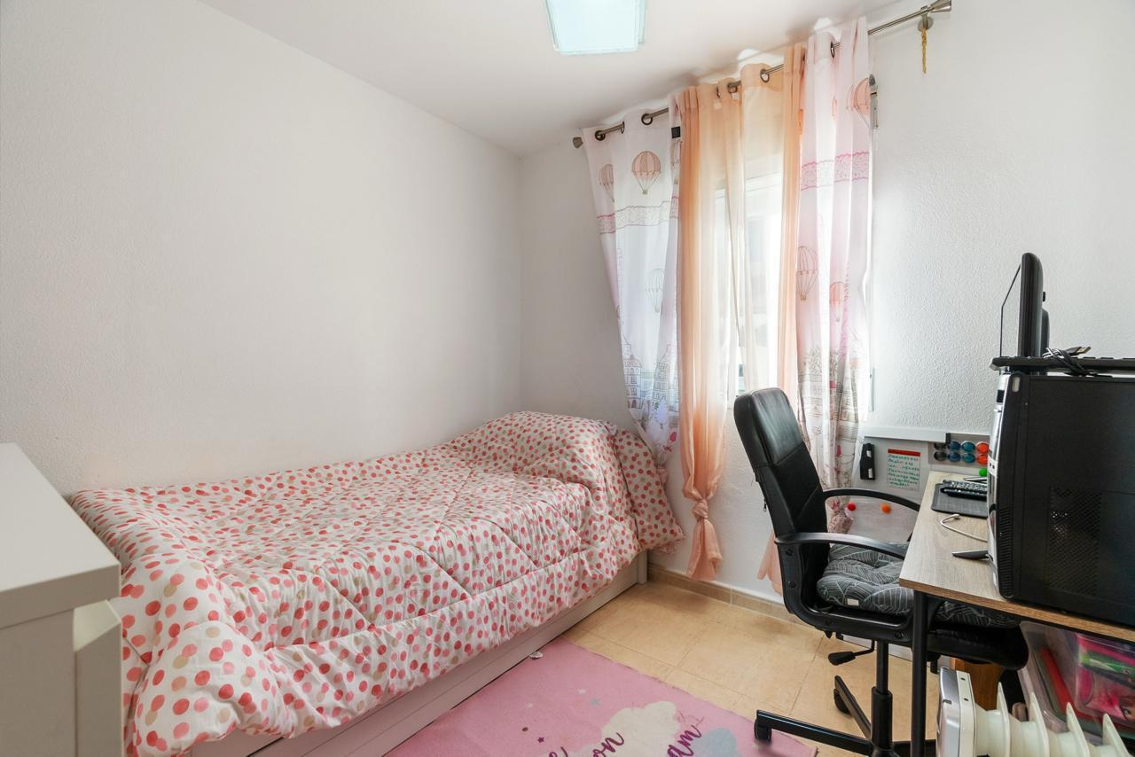 Small bedroom with a single bed along the left wall, pink dotted bedding, and sheer pink curtains by the window opposite a desk and computer.