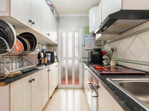 Narrow galley kitchen with a dish rack and stacked pots on the left, stove and sink on the right, door at the end with frosted panels.