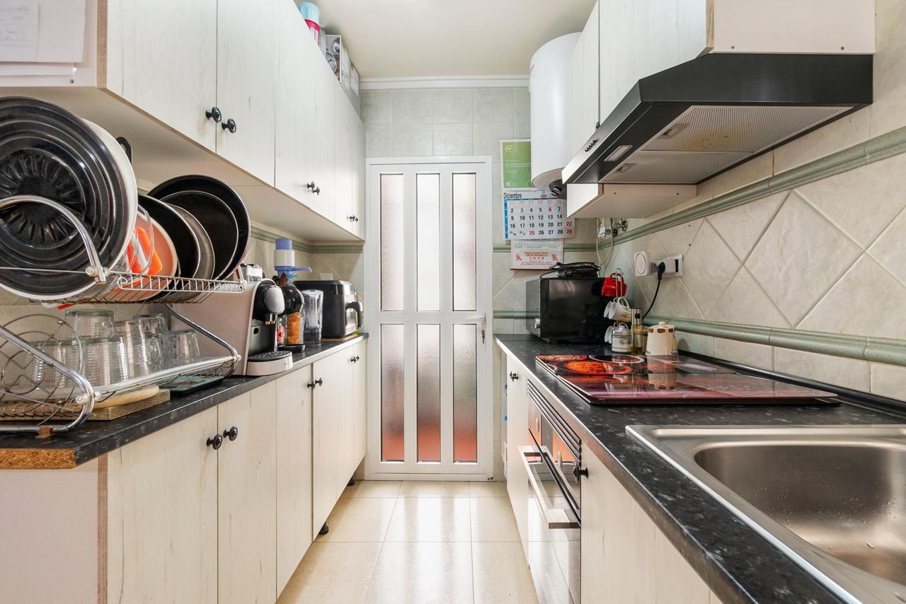 Narrow galley kitchen with a dish rack and stacked pots on the left, stove and sink on the right, door at the end with frosted panels.