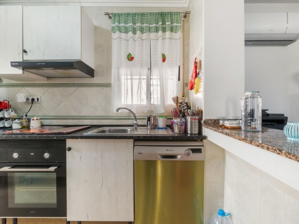 Kitchen scene with sink under a window, a stainless dishwasher, and a black oven beside white cabinets.