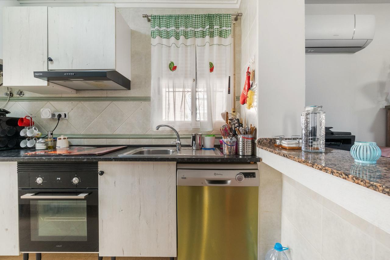 Kitchen scene with sink under a window, a stainless dishwasher, and a black oven beside white cabinets.