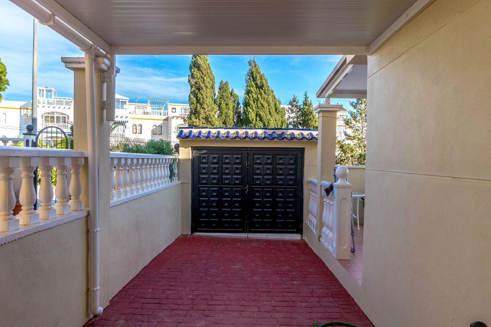 Residential courtyard with a black double gate at the end of a red brick driveway and white balustrades on both sides.