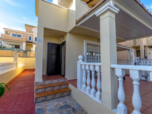 Beige house exterior with white decorative railing, tiled steps, and a covered entrance courtyard.