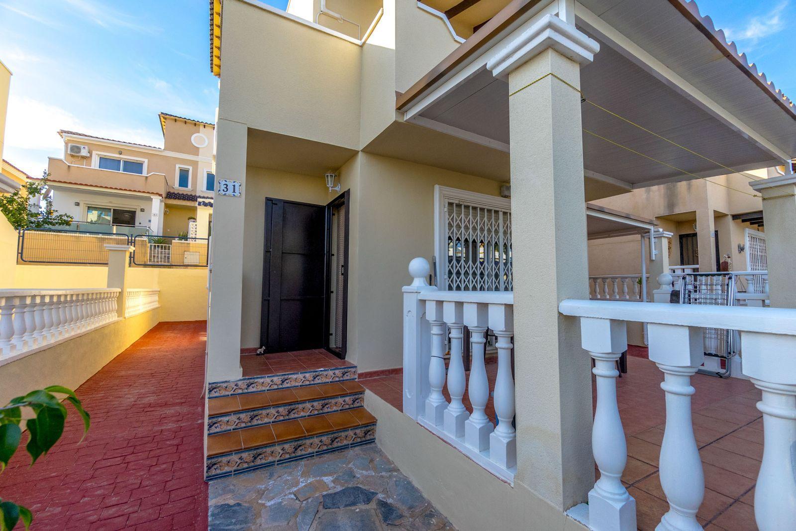 Beige house exterior with white decorative railing, tiled steps, and a covered entrance courtyard.