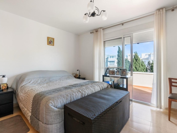 Bright modern bedroom with a large bed, gray bedding, two black nightstands, and a woven bench at the foot.