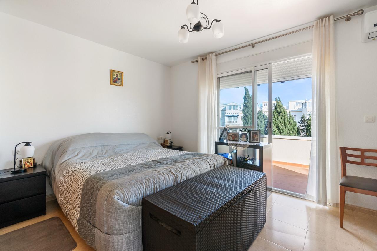 Bright modern bedroom with a large bed, gray bedding, two black nightstands, and a woven bench at the foot.