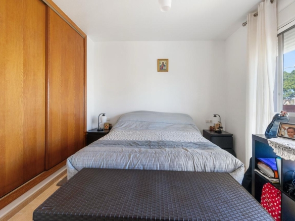 Bed centered against white wall with two dark nightstands, lamps, and a wooden wardrobe on the left; window with white curtains on the right.