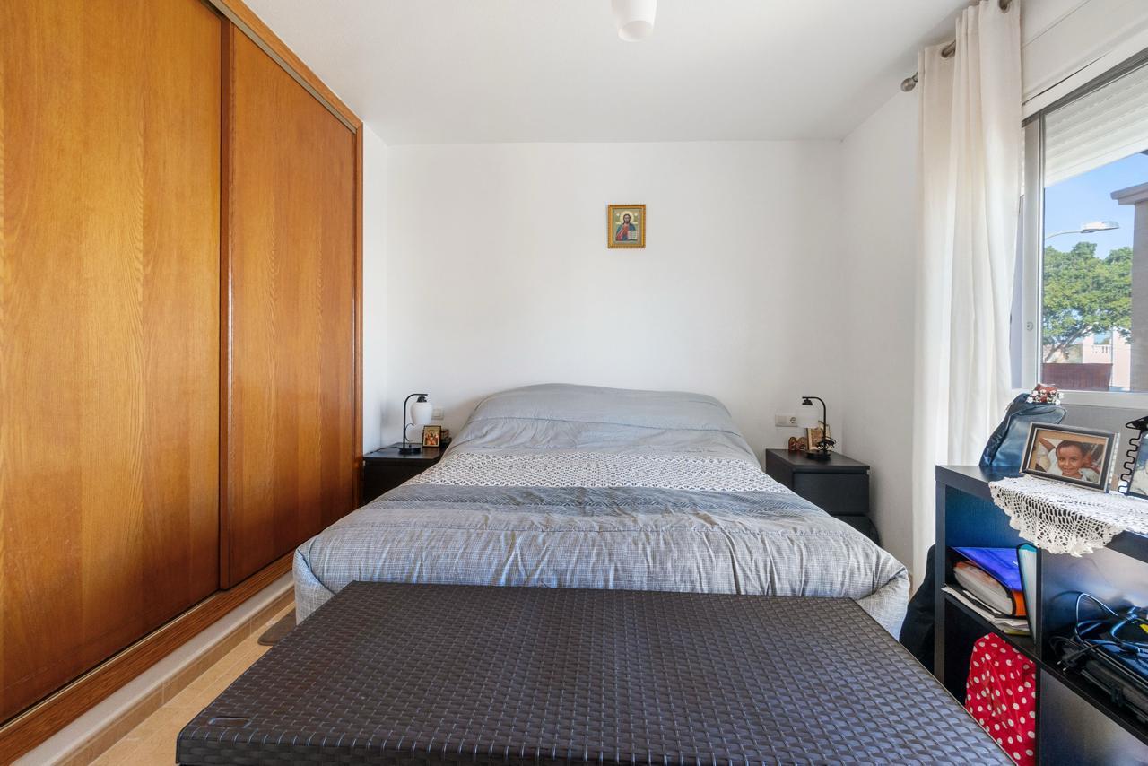 Bed centered against white wall with two dark nightstands, lamps, and a wooden wardrobe on the left; window with white curtains on the right.