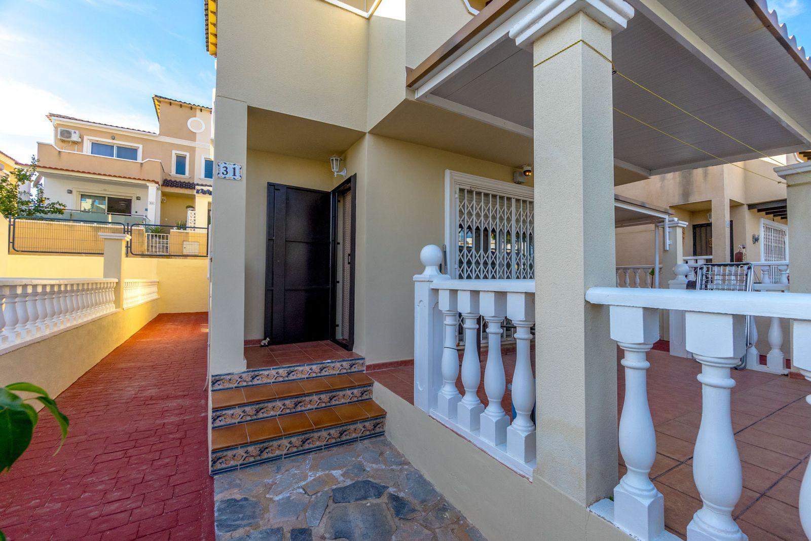 Front entrance of a beige two-story home with white balustrade, tiled steps, and a black front door