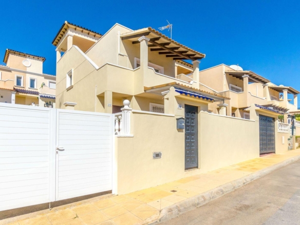 Row of beige Mediterranean townhouses behind white gates on a sunny street with a bright blue sky behind them.