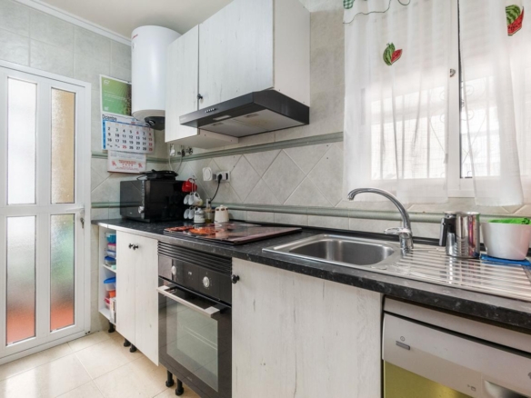 Narrow kitchen with white cabinets, black countertop, and a sink by a window; appliances include oven, microwave, and dishwasher.