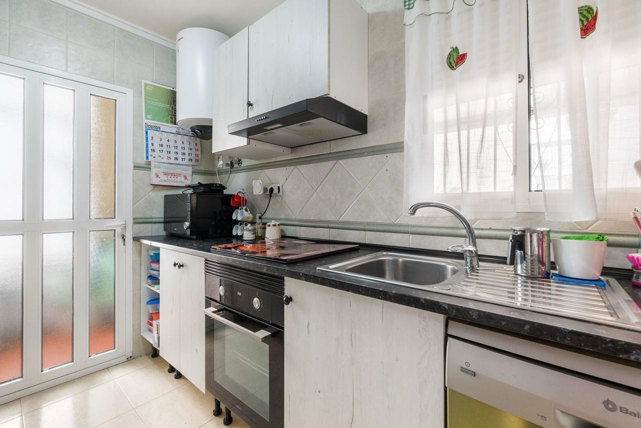 Narrow kitchen with white cabinets, black countertop, and a sink by a window; appliances include oven, microwave, and dishwasher.