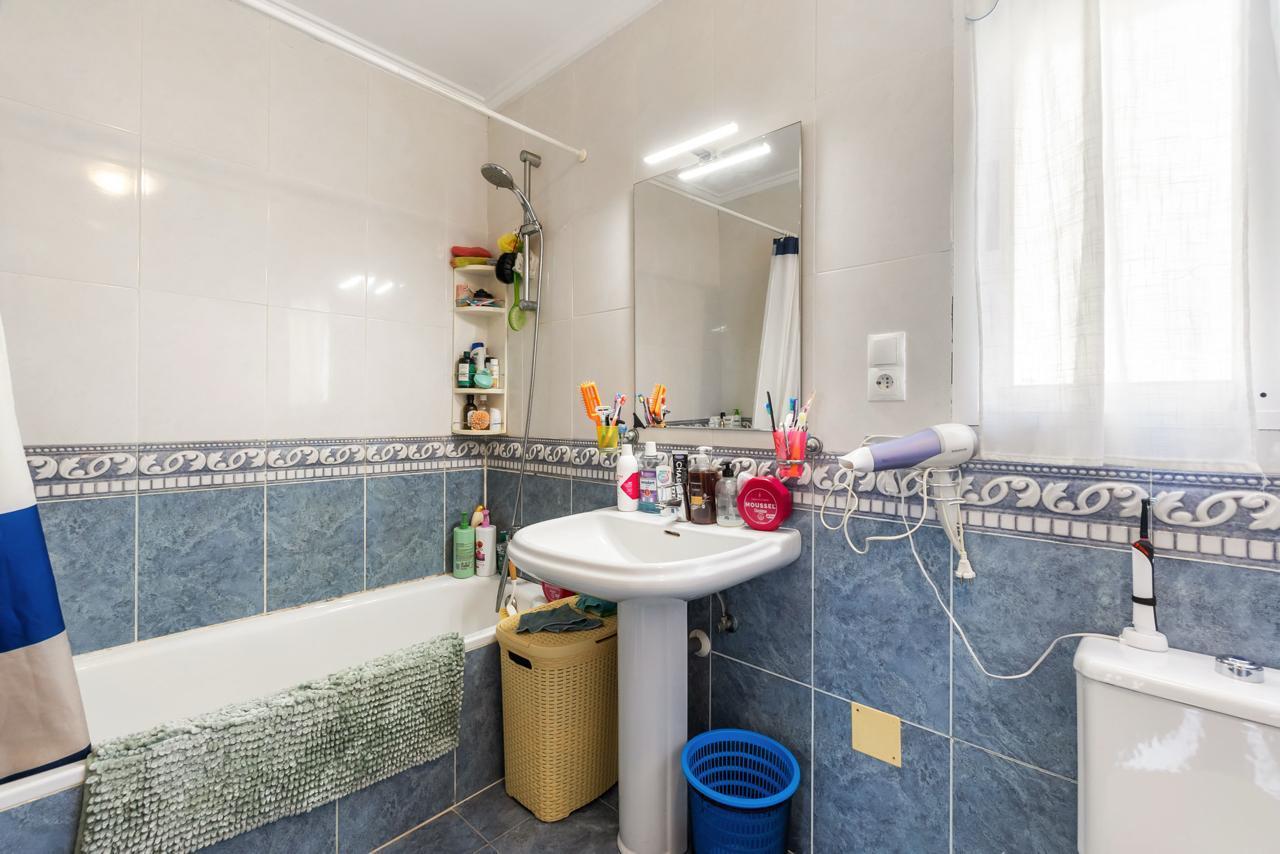 Small bathroom with a pedestal sink, mirror, and bathtub; toiletries line the tub edge and a towel hangs over the tub side.
