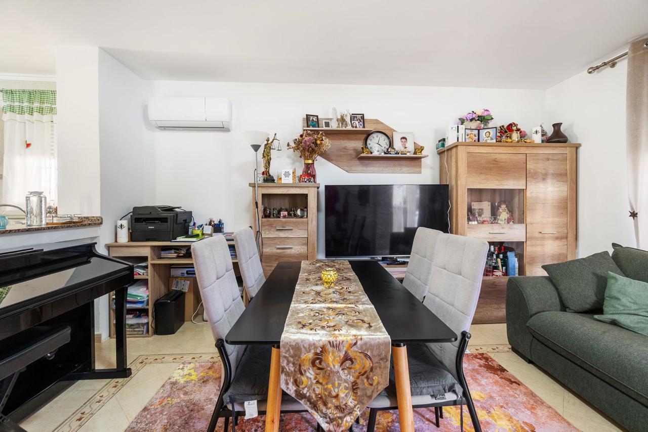 Modern living room with a black dining table, six gray upholstered chairs, and a large TV on a wooden stand behind them.