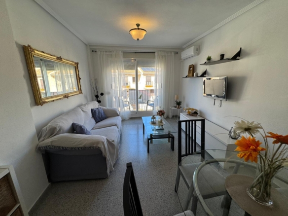 Bright living room with a white sofa, glass coffee table, and balcony door behind sheer curtains.