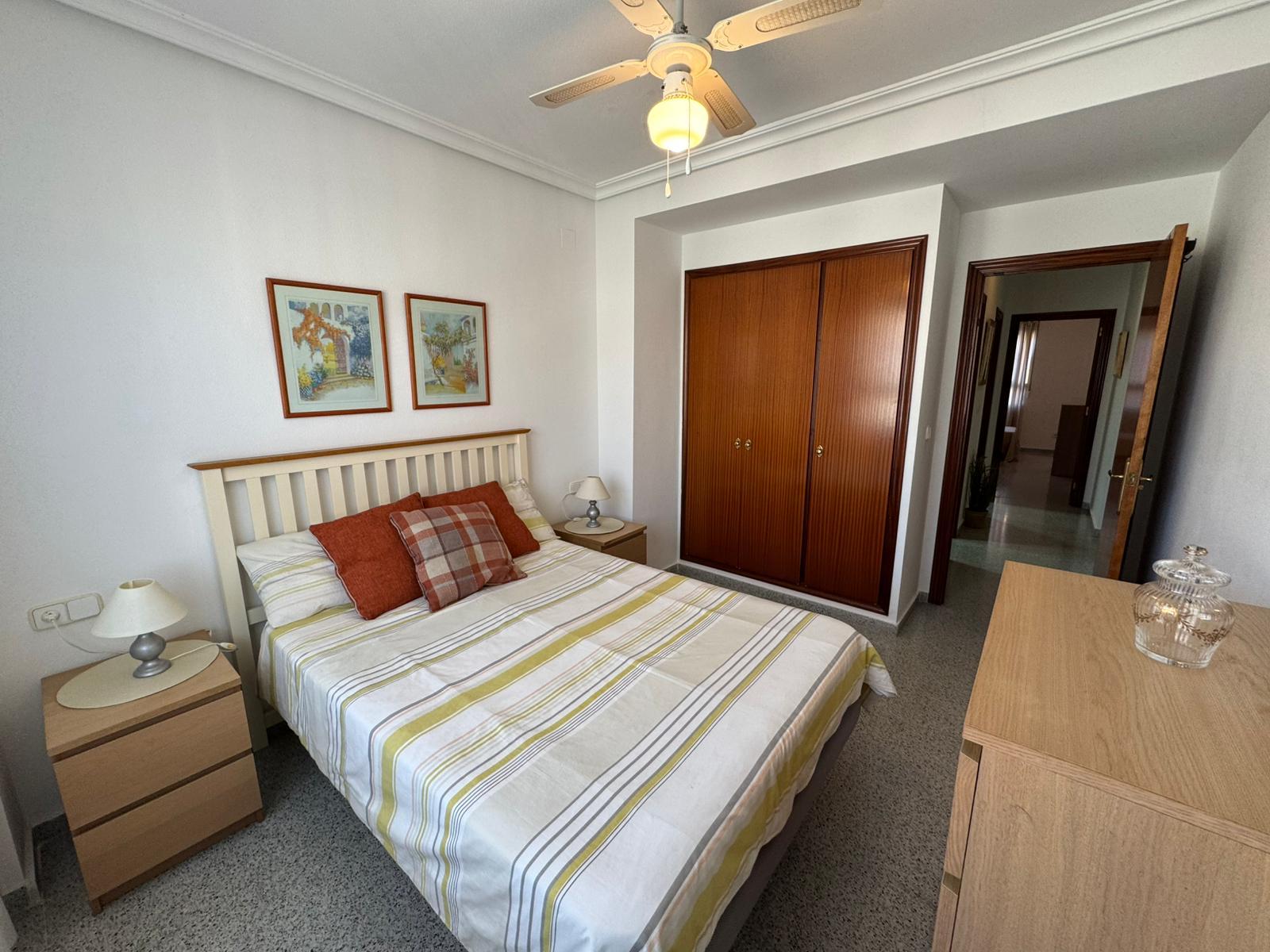 Bedroom with a double bed, striped comforter and red plaid pillows, two wooden nightstands, and a ceiling fan above.