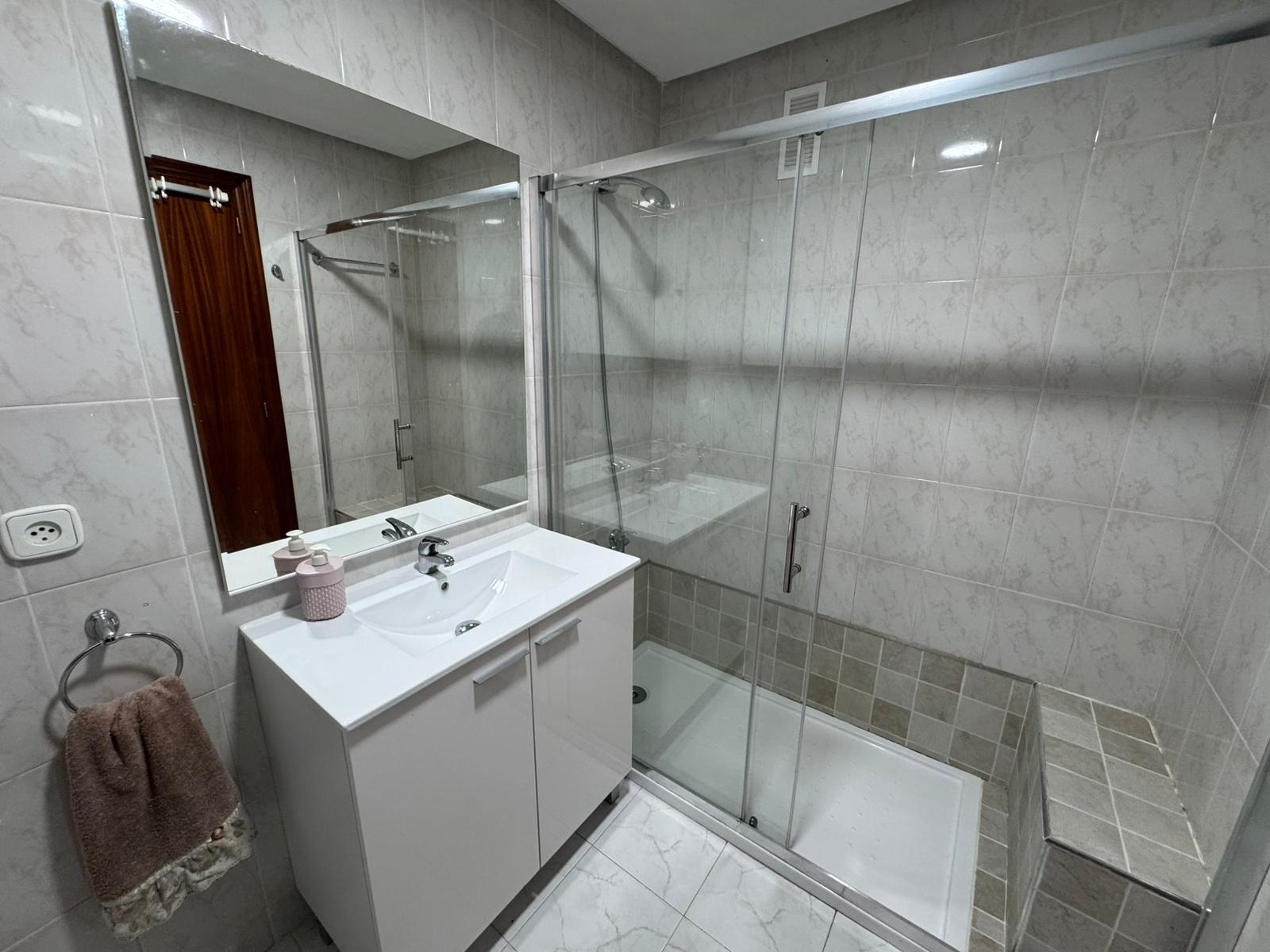 White bathroom with a vanity sink, large mirror, and a glass-enclosed shower.