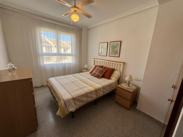 A small bedroom with a wood bed, two nightstands, and a dresser, sunlight streaming through sheer curtains by a window.