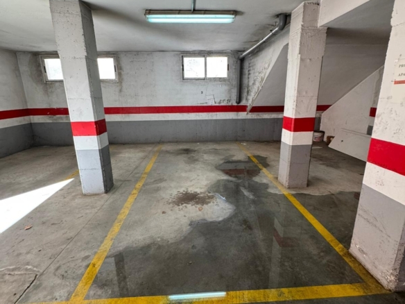 Empty indoor parking garage with concrete pillars painted gray and red, yellow stall lines, and a wet floor.