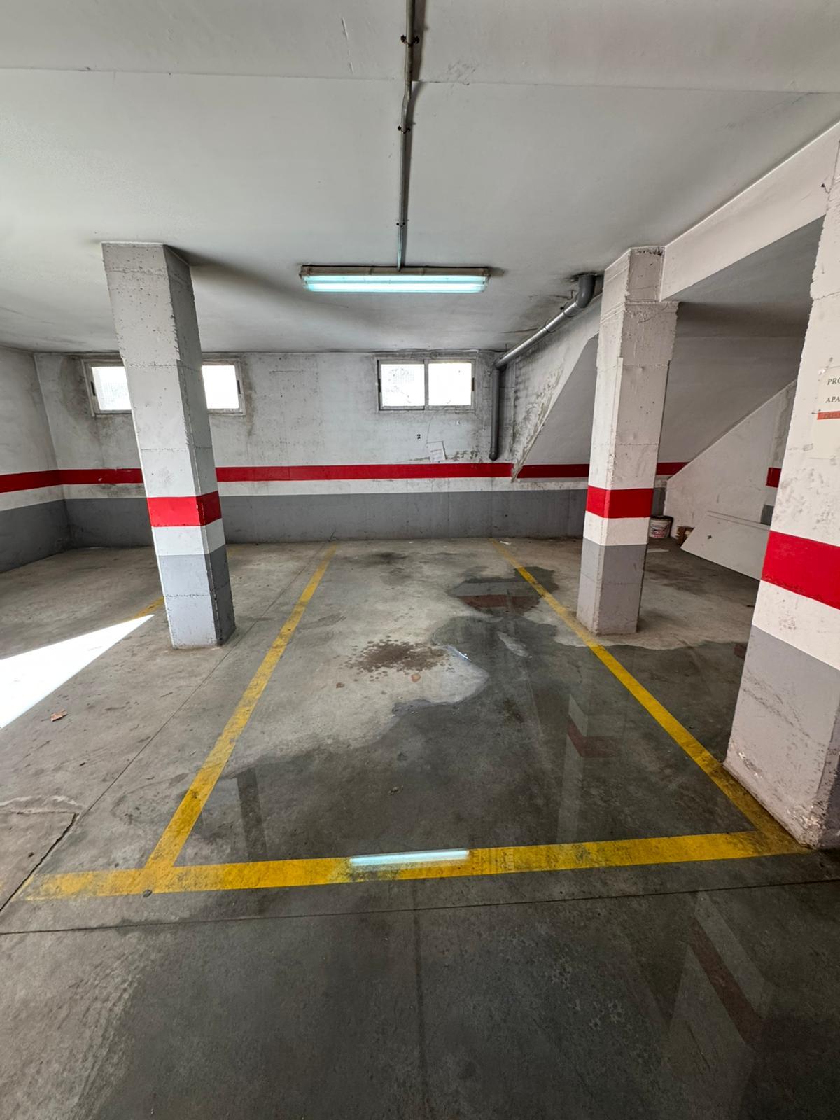Empty indoor parking garage with concrete pillars painted gray and red, yellow stall lines, and a wet floor.