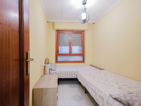 Small yellow bedroom with two single beds, a wooden dresser, and a window with blinds.