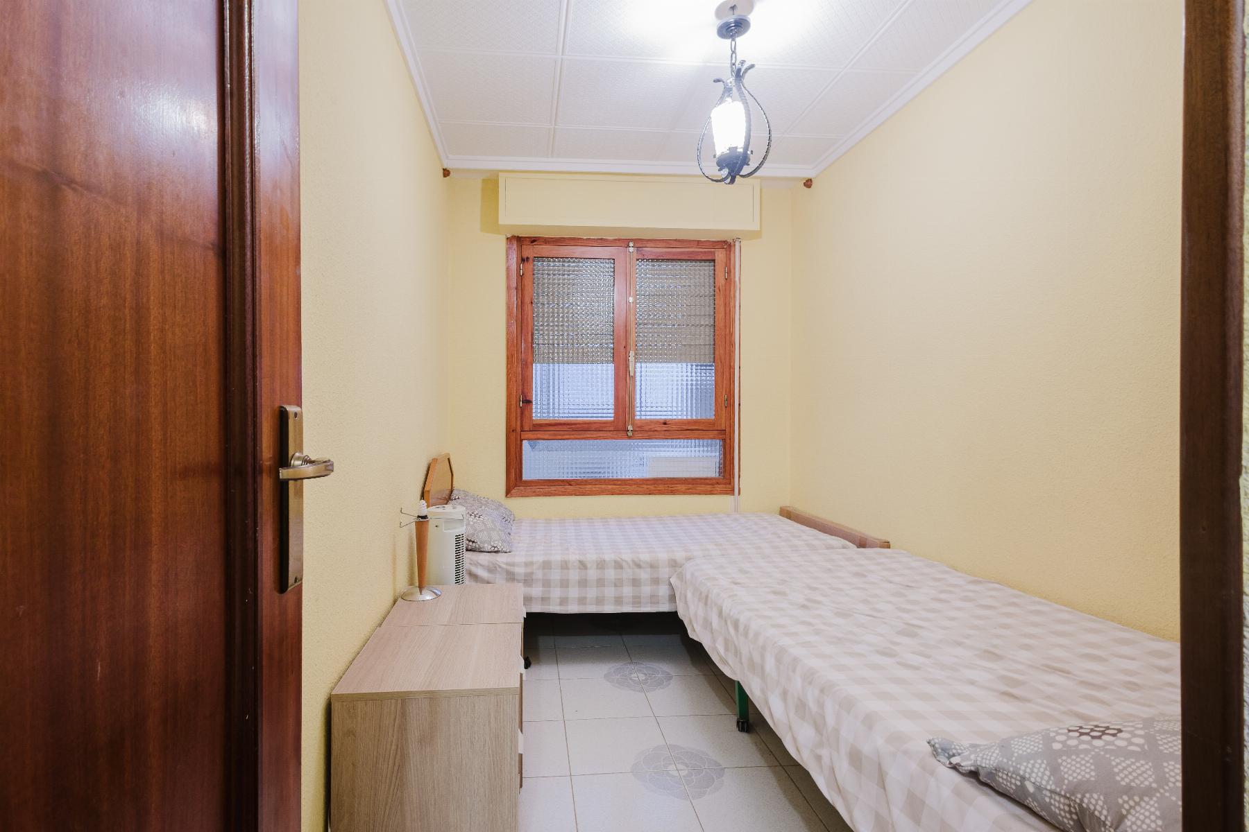Small yellow bedroom with two single beds, a wooden dresser, and a window with blinds.