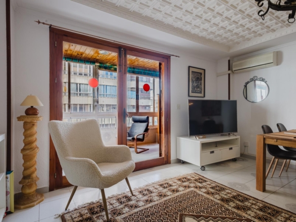 Living room with cream upholstered chairs facing glass doors to a balcony, a patterned rug, and a TV on a white stand.
