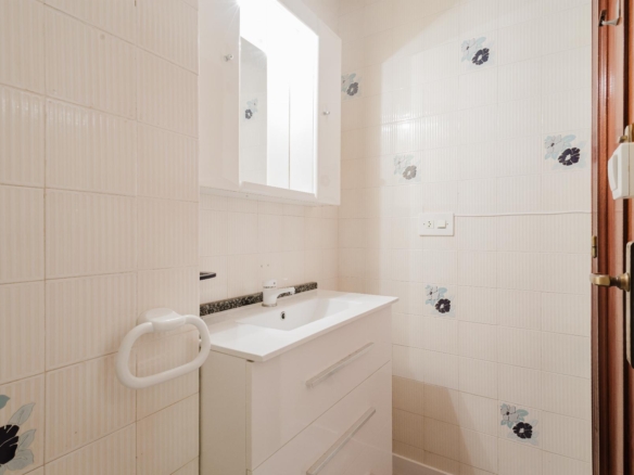 Small white bathroom with a sink, cabinet mirror, and tiled walls featuring blue floral accents.