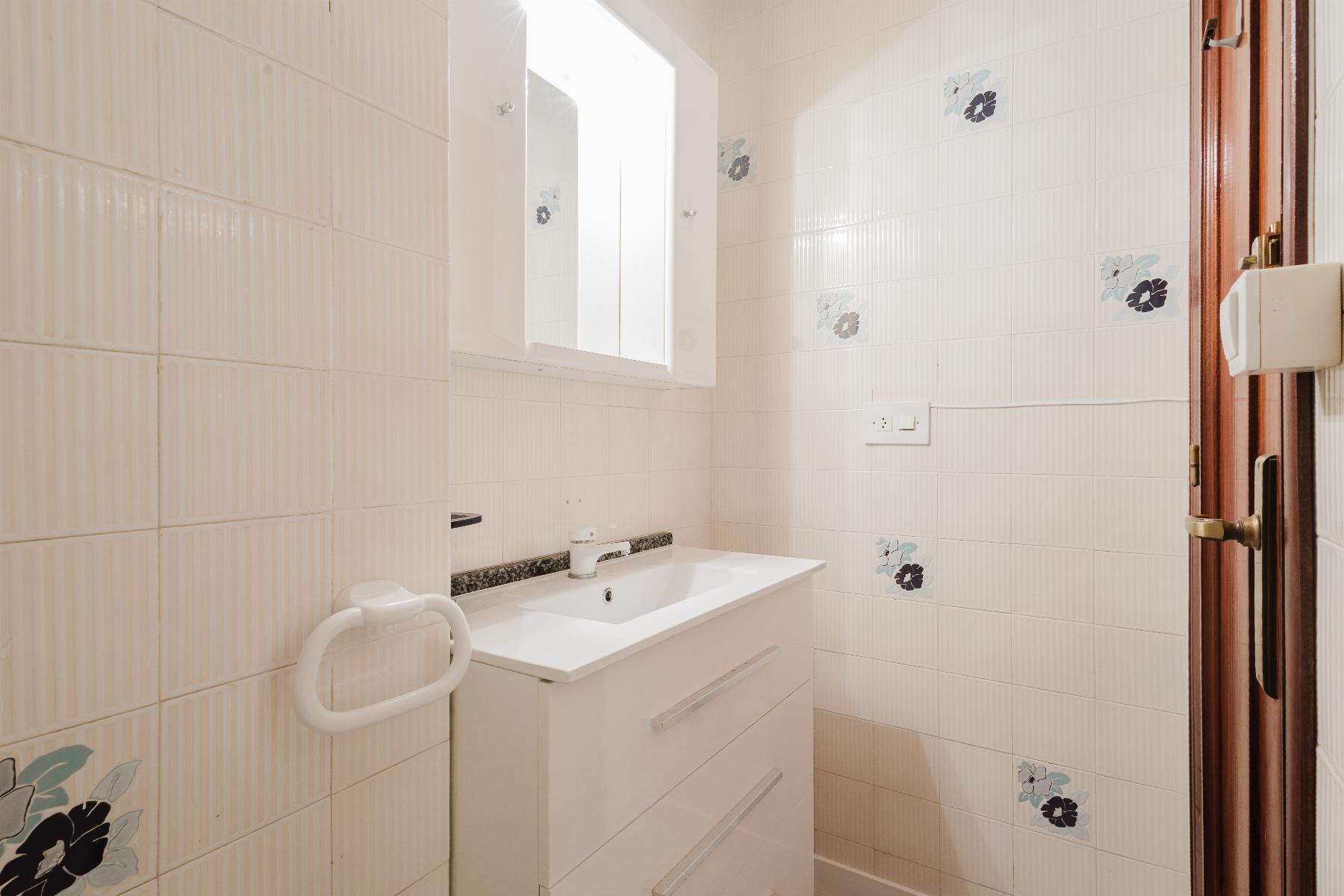 Small white bathroom with a sink, cabinet mirror, and tiled walls featuring blue floral accents.