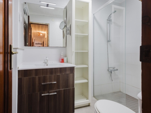 Modern bathroom with a dark wood vanity, white countertop, and tall white cabinet next to a glass-enclosed shower.