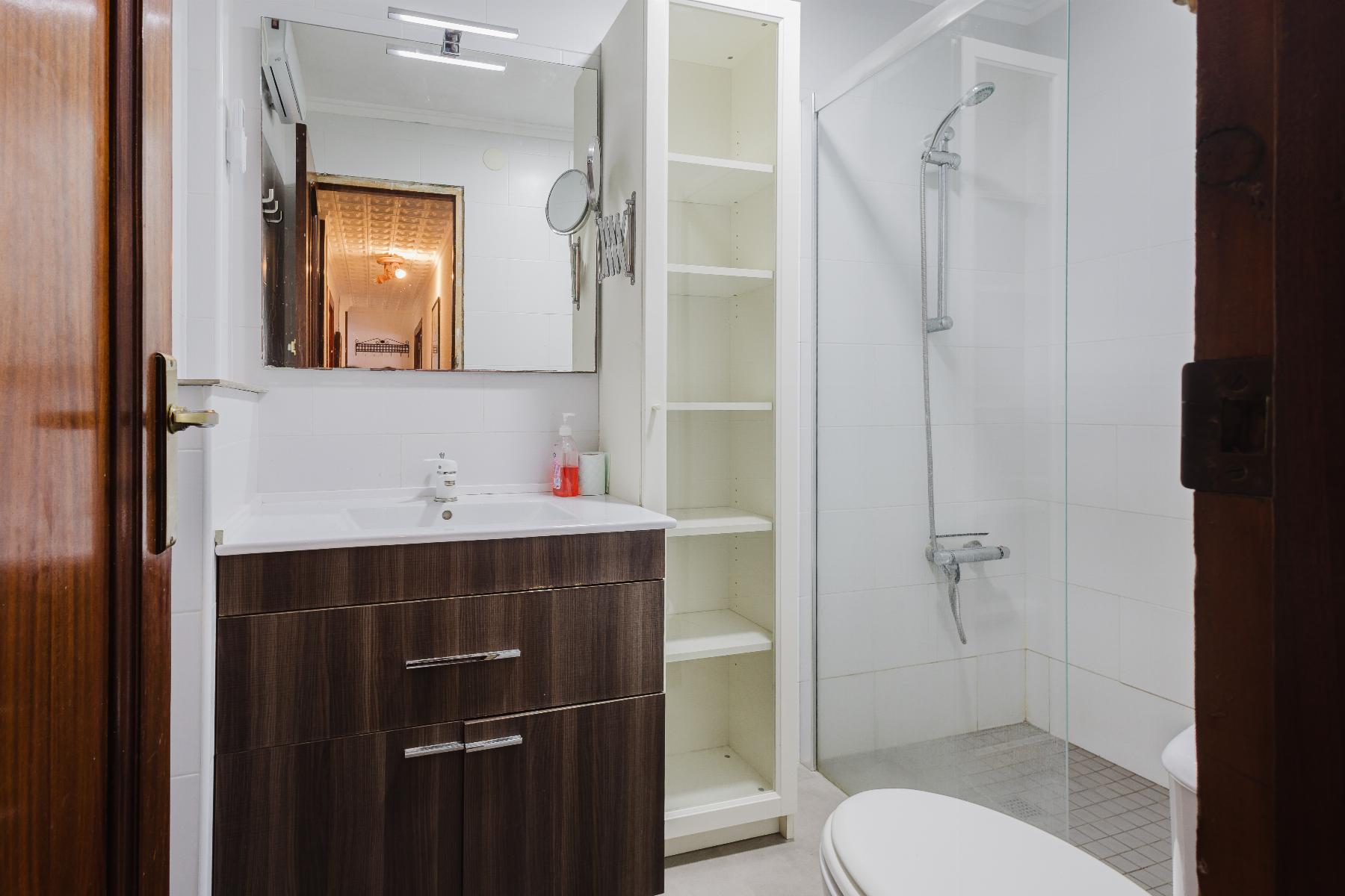 Modern bathroom with a dark wood vanity, white countertop, and tall white cabinet next to a glass-enclosed shower.