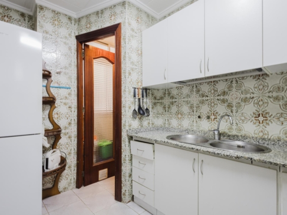 White kitchen with granite countertop, double sink, and wall-to-wall white cabinets next to a wooden-framed doorway with patterned tile wallpaper surrounding it.
