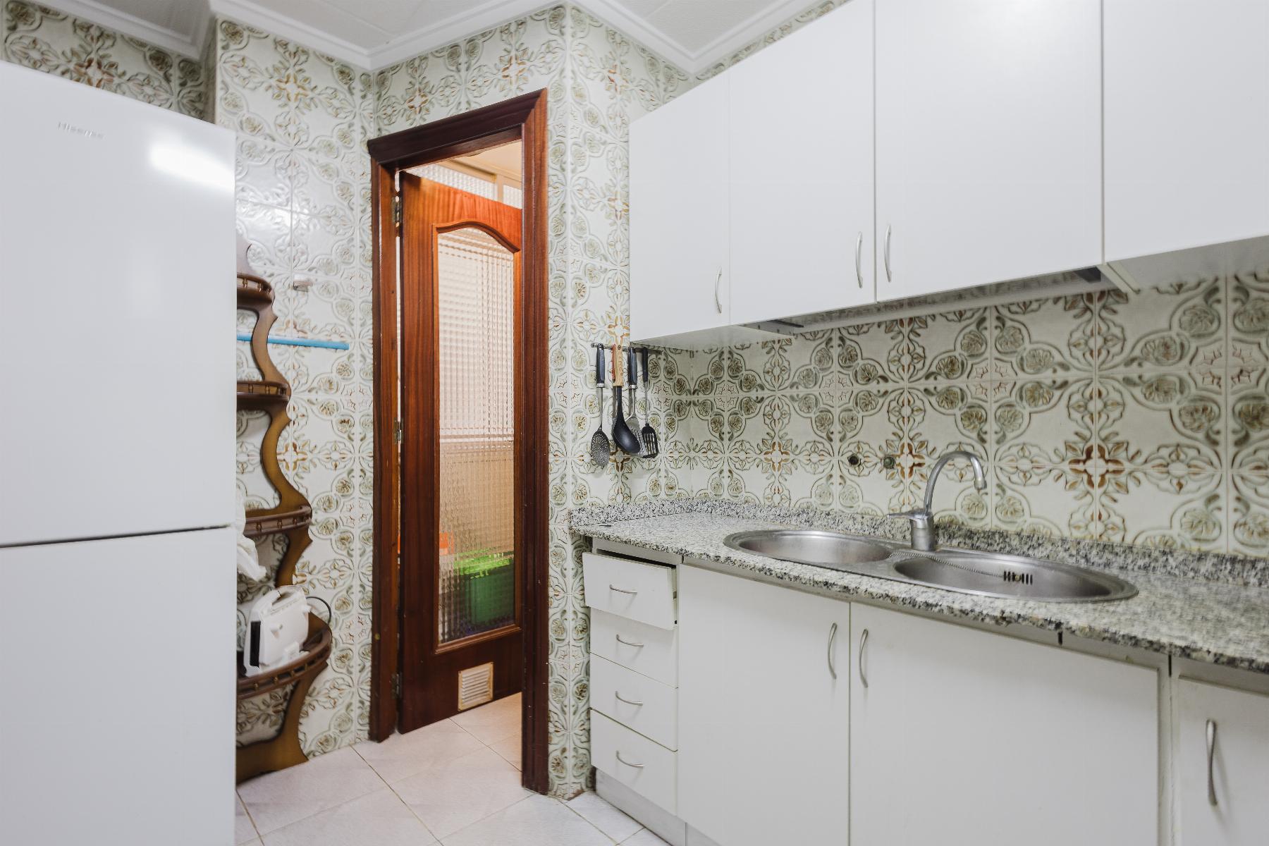 White kitchen with granite countertop, double sink, and wall-to-wall white cabinets next to a wooden-framed doorway with patterned tile wallpaper surrounding it.