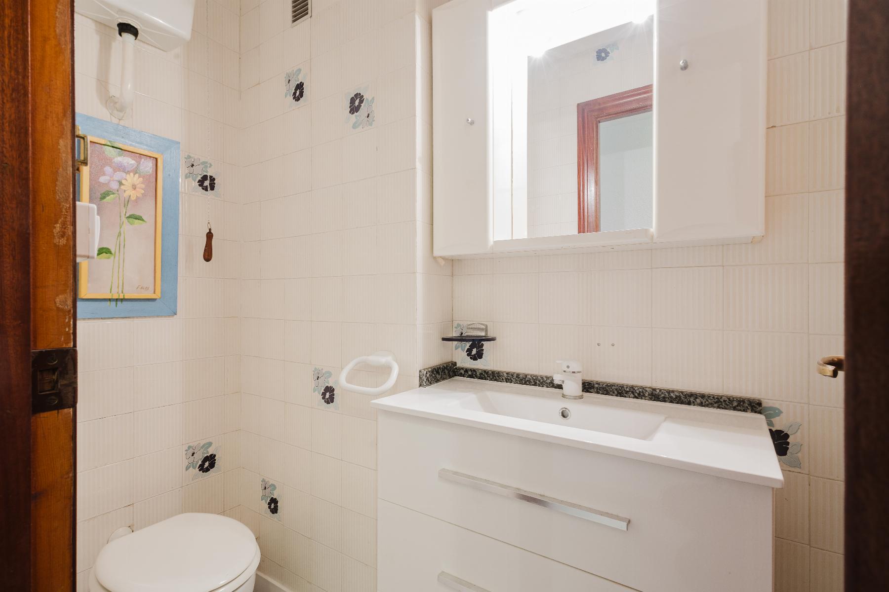 Small white bathroom with a vanity sink, mirrored cabinet, and toilet, tiled walls with floral accents on the tiles.