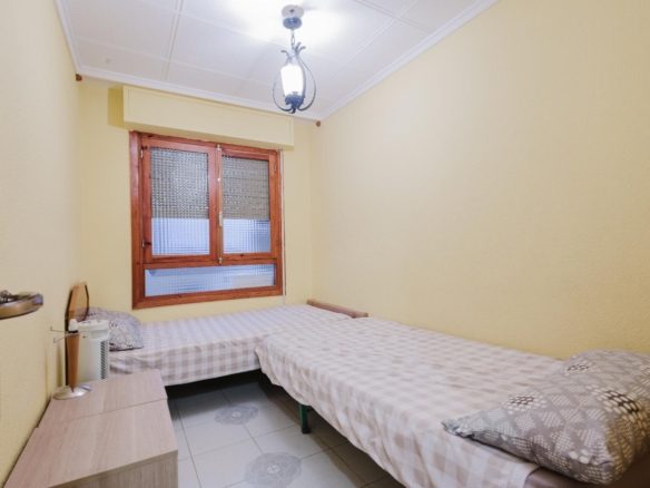 Twin bedroom with two single beds, gray-and-white checkered bedding, yellow walls, and a wooden-framed window under a ceiling lantern.