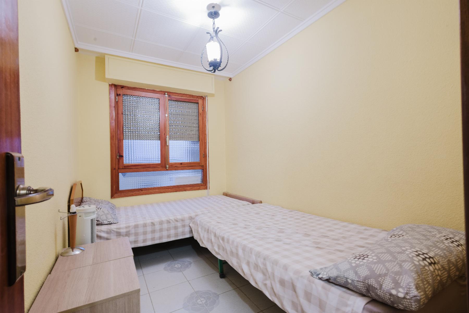 Twin bedroom with two single beds, gray-and-white checkered bedding, yellow walls, and a wooden-framed window under a ceiling lantern.