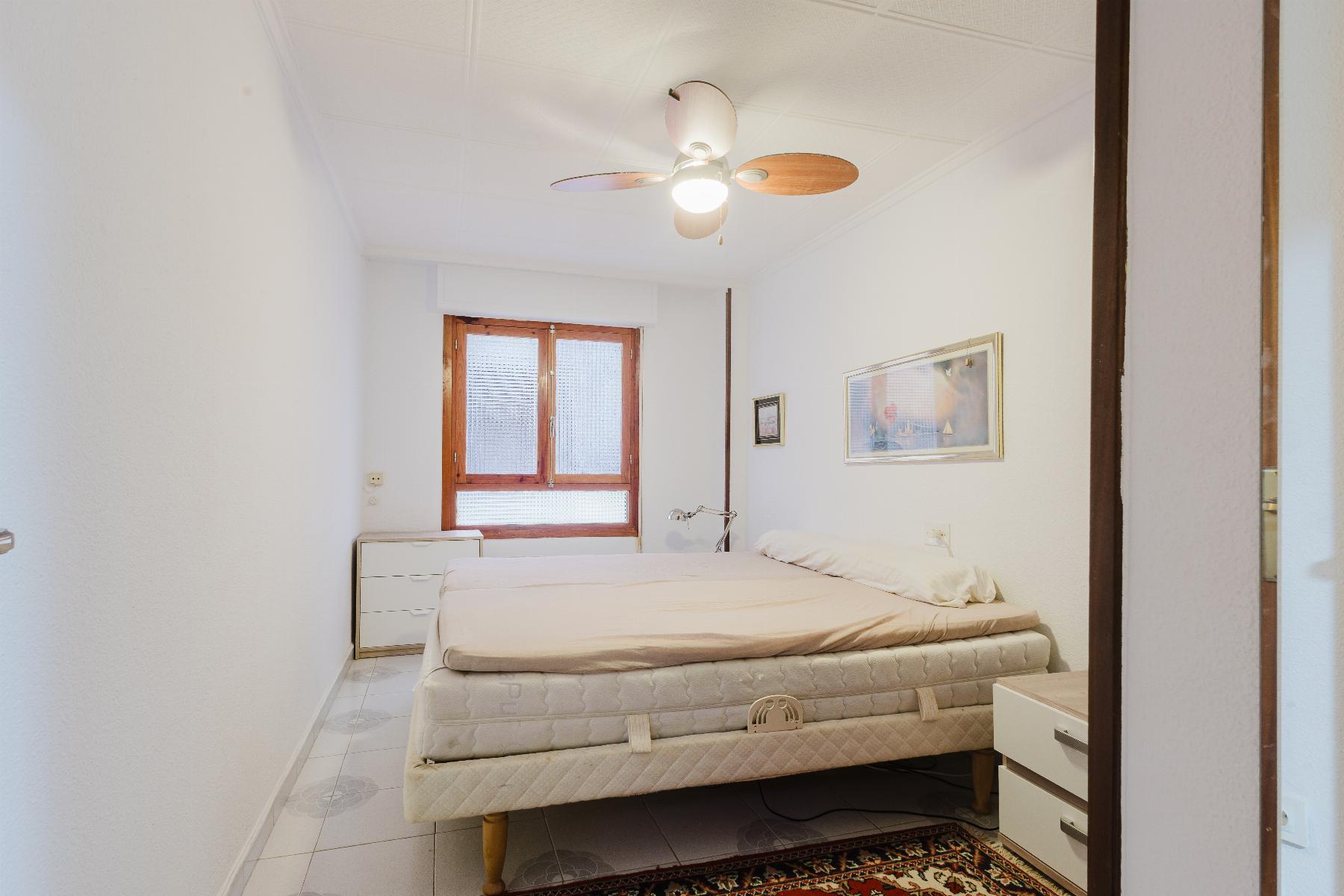 Small bright bedroom with stacked mattresses on a bed, ceiling fan, and a wooden-framed window.