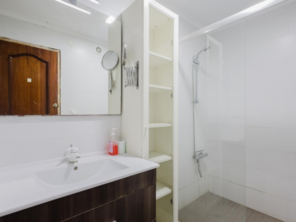 Modern white bathroom with a dark wood vanity, wide mirror, and glass shower enclosure.