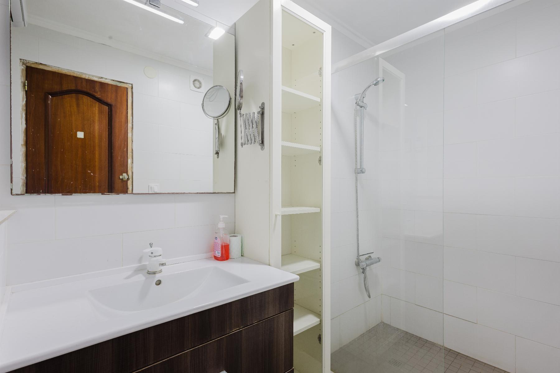 Modern white bathroom with a dark wood vanity, wide mirror, and glass shower enclosure.